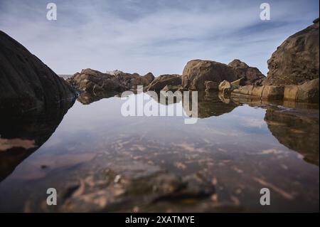 Eine ruhige Landschaft mit großen Felsformationen, die sich in ruhigem Wasser unter einem klaren, blauen Himmel spiegeln. Die Szene fängt die Schönheit der Natur in einer Pässe ein Stockfoto