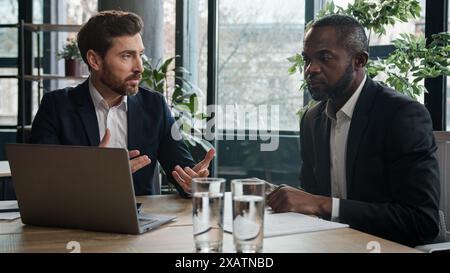 Zwei verschiedene Geschäftsleute, multirassische Männer im Büro mit Laptop. Kaukasischer Finanzberater Manager Berater Versicherungsagent Beratung Afrikaner Stockfoto