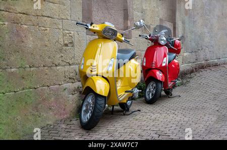 Zwei Vintage-Motorräder in gelber, roter Farbe, die auf gepflastertem Bürgersteig geparkt sind, Steinmauerhintergrund. Altmodisches Motorrad, Moped, Transportfahrzeug. Stockfoto