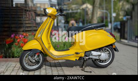 Motorroller Vintage gelb Farbe Motorrad geparkt auf gepflastertem Bürgersteig, verschwommener Stadthintergrund. Altmodisches Motorrad, Moped, Transportfahrzeug. Stockfoto
