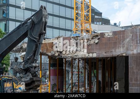 Gebäudeabbruchkonzept. Bagger vor halb zerstörtem Gebäude auf der Baustelle, neuer Baugrund vor Altbau rui Stockfoto