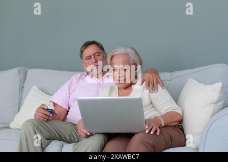 Ältere Ehepaare kaufen online mit einer Kartenbank ein, indem sie einen Laptop benutzen Stockfoto