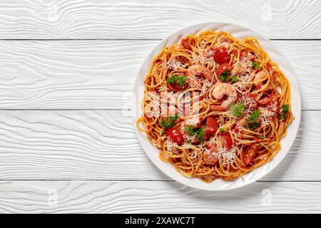 Garnelen fra diavolo mit Spaghetti, Tomatensoße, bestreut mit geriebenem Parmesankäse auf weißer Platte auf weißem Holztisch, horizontale Ansicht Stockfoto