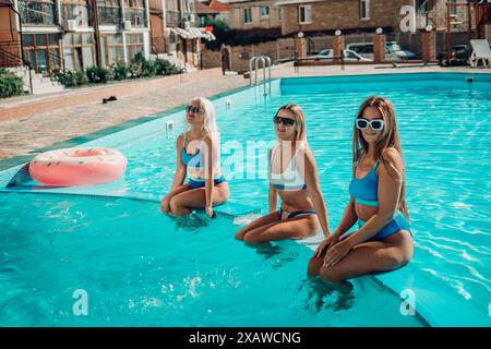 Drei Frauen sitzen in einem Pool mit rosafarbenen und blauen Schwimmbahnen. Die Szene ist unbeschwert und lustig Stockfoto