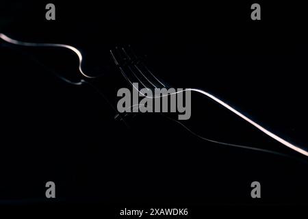 Zwei ineinander greifende glänzende Gabeln auf reflektierendem schwarzem Hintergrund für künstlerisches minimalistisches Stillleben oder Konzept mit schattenhafter Reflexion. Stockfoto