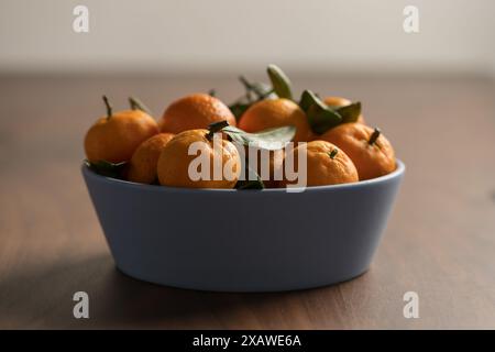 Kleine organische Mandarinen mit Blättern in Keramikschale auf Holztisch, flacher Fokus Stockfoto