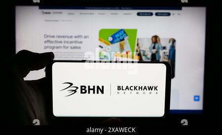 Person, die ein Mobiltelefon mit dem Logo des Zahlungslösungsunternehmens Blackhawk Network Holdings Inc. Vor der Webseite hält. Schwerpunkt auf dem Display des Telefons. Stockfoto