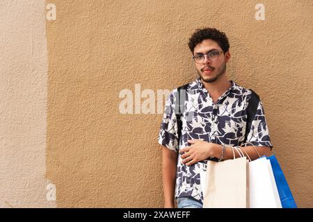 Die Stadt erkunden: Junger Mann in bedruckten Hemden und Einkaufstaschen. Urbaner Stil, Mode, Erkundung Stockfoto
