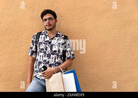 Junger Mann mit Rucksack und bedrucktem Hemd auf der Suche und im Ruhezustand. Mode, Lifestyle, urbane Entdeckungen Stockfoto