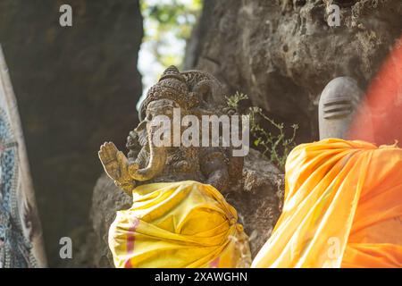 Eine Steinstatue der hinduistischen Gottheit Ganesha, mit gelbem Tuch bedeckt, in einem felsigen Außenbereich aufgestellt. Stockfoto