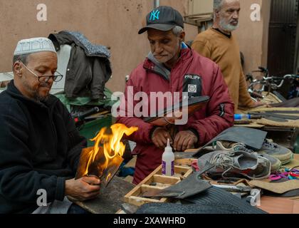 Marrakesch, Marokko - 23. März 2024: Traditionelle Schuhmacher im Souk der Medina von Marrakesch kleben neue Sohlen auf alte Schuhe Stockfoto