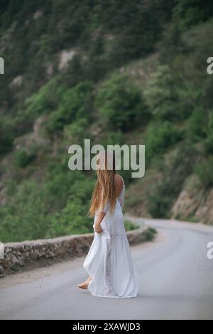 Eine Frau in einem weißen Kleid läuft die Straße entlang. Die Straße ist eine unbefestigte Straße mit Bäumen im Hintergrund. Die Frau ist allein und trägt ein langes Kleid Stockfoto