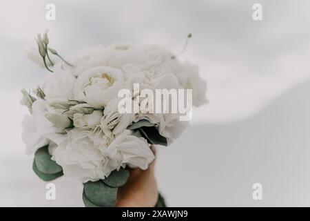 Ein Strauß weißer Blumen wird von einer Person gehalten. Die Blumen sind so angeordnet, dass sie aussehen wie in einer Vase. Der Blumenstrauß ist der mai Stockfoto