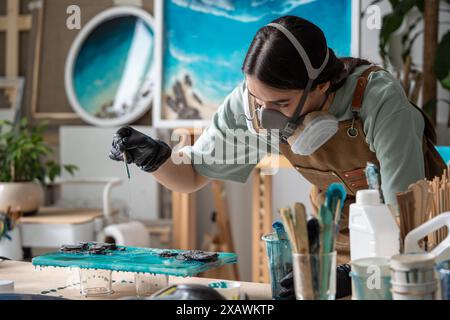 Aufmerksame, gründliche Frau, die sorgfältig mit Epoxidharz arbeitet, um Kunstwerke zu malen. Stockfoto