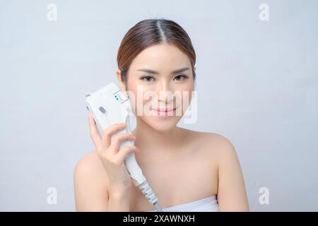 Entzückende asiatische Frau, die Laser-HIFU-Gerät für Gesichtsheben zeigt Stockfoto