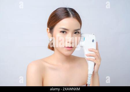 Schöne asiatische Frau, die Laser-HIFU-Gerät für Gesichtsstraffung hält Stockfoto