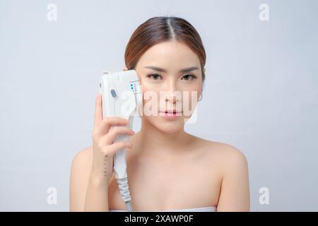 Elegante asiatische Frau mit Laser-HIFU-Gerät zum Anziehen des Gesichts Stockfoto