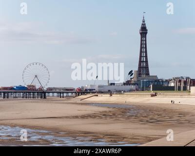 Menschen sitzen auf der Promenade neben dem Sandstrand und Blackpool Tower in der Stadt Blackpool, Lancashire, England. Juni 2024 Stockfoto