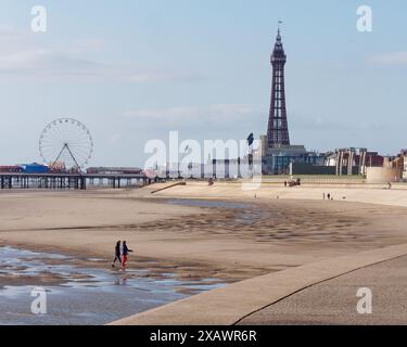 Touristen wandern am Sandstrand neben dem Blackpool Tower in der Stadt Blackpool, Lancashire, England. Juni 2024 Stockfoto