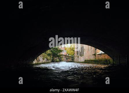 Eine ruhige Bootsfahrt durch den Kanal von Brügge mit zwei malerischen Brücken in der Ferne Stockfoto