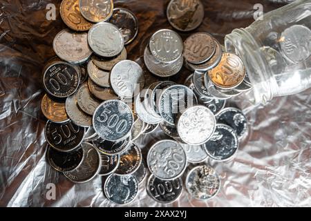 Ein Stapel südkoreanischer Münzen, darunter 500 und 100 Won-Stückelungen, die aus einem Glasgefäß auf eine zerknitterte metallische Oberfläche geschüttet wurden. Stockfoto