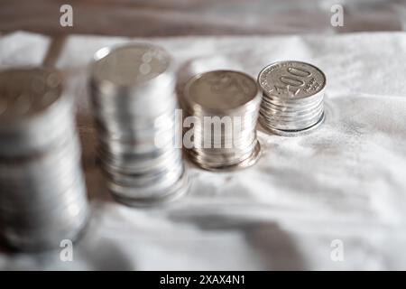 Stapel von Silbermünzen auf einer weißen Oberfläche, einige Stapel sind im Vordergrund verschwommen und ein Stapel im Fokus. Stockfoto