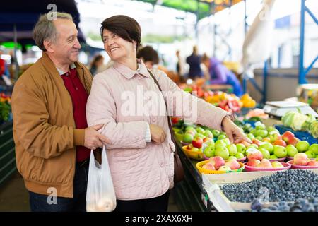 Glückliches, reifes Paar, das frische Blaubeeren pflückt, während wir zusammen auf dem lokalen Markt einkaufen Stockfoto