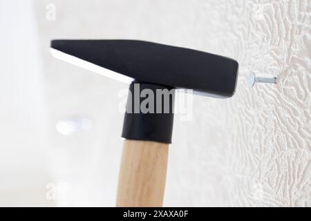 Hammerhämmer Nagel in weiße Wand zu Hause Nahaufnahme Stockfoto