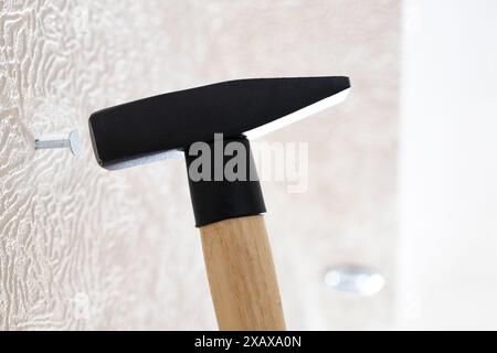 Der Hammer treibt den Nagel in die weiße Wand zu Hause aus nächster Nähe Stockfoto