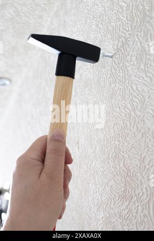 Männliche Hand mit Hammer treibt Nagel in die weiße Wand iat nach Hause Stockfoto