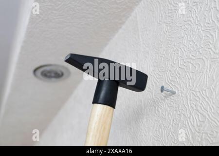 Hammerhämmer nageln sich zu Hause in die weiße Wand Stockfoto