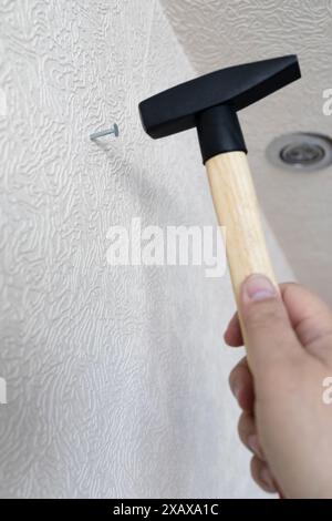 Männliche Hand mit Hammerhämmern, die im Haus in die Wand nageln Stockfoto