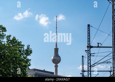 Ein hoher Turm mit einer roten Spitze steht vor einem blauen Himmel. Der Turm ist von Bäumen und Drähten umgeben Stockfoto