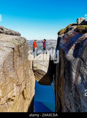 Zwei Personen stehen auf einer Felsbrücke mit Blick auf eine atemberaubende norwegische Landschaft, scheinbar in der Luft. Ein paar Männer und Frauen besuchen Kjeragbolten, Norwegen Stockfoto