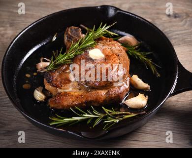 Schweinekotelett auf dem Knochen in einem Stück Butter mit Knoblauch und Rosmarin in einer Pfanne Stockfoto