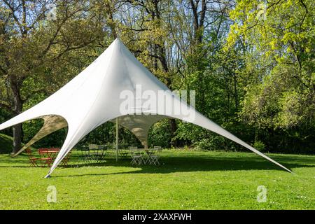 Großes weißes Pavillonzelt mit Gartenstühlen und Tischen in einem Park Stockfoto