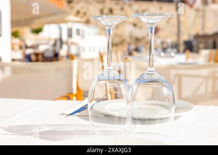 Saubere, umgedrehte Weingläser warten an einem gedeckten Tisch vor einem Restaurant in einem Ferienresort an einem schönen sonnigen Tag auf Gäste Stockfoto