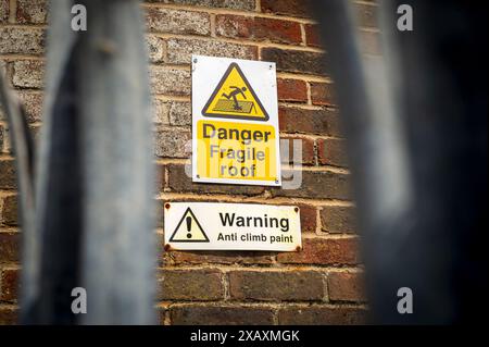 Warnschild mit Anti-Climb-Farbe und zerbrechlichem Dach an der Seite eines Gebäudes. Stockfoto