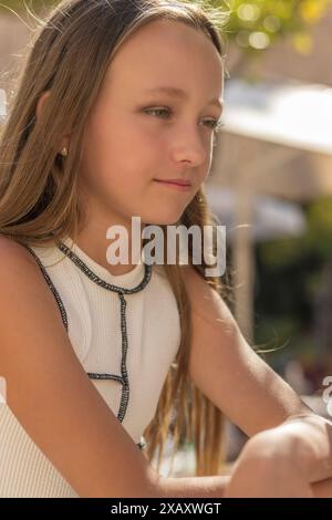 Dieses Bild zeigt ein Porträt eines jungen Mädchens mit langen blonden Haaren, das in Sonnenlicht getaucht ist und ihre goldenen Locken hervorhebt. Stockfoto