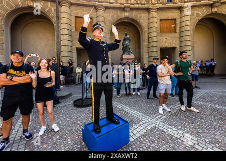 Der Dirigent der Kavallerie-Band steht auf einer Plattform inmitten der Touristen und leitet das Konzert mit Marschmusik und Abba-Liedern. Zeremonie der Kaisergarde im Königspalast von Stockholm. Wachwechsel vor dem schwedischen Königspalast in Stockholm mit musikalischer Begleitung der berittenen Band. Yttre borggården, Stockholm, Schweden Stockfoto