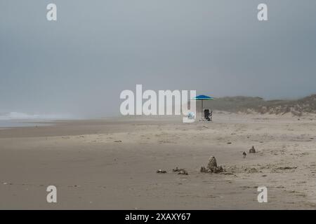 Sonnenschirm mit Stühlen hinter Sandburgen am leeren Sandstrand am Cape Hatteras in North Carolina, USA Stockfoto