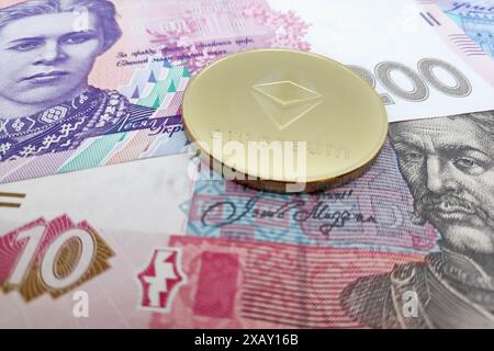 Nahaufnahme einer goldenen Ethereum-Münze auf einem Stapel ukrainischer Hrywnja-Banknoten. Stockfoto