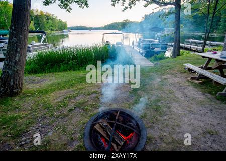Rauch zieht auf einen See von Wisconsin, während die heißen Kohlen bei Sonnenuntergang rot leuchten. Fischerboot im Hintergrund. Stockfoto