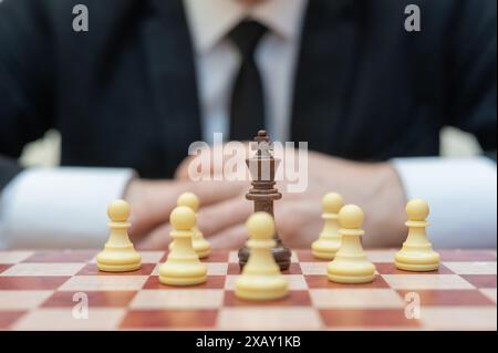 Ein würfeliger Mann ist hinter einem Schachbrett mit einem König umgeben von Bauern. Stockfoto