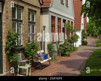 Reihenhäuser mit roten Ziegeldächern, grüner Vegetation und einer Bank auf einer Kopfsteinpflasterstraße, Arnis, Schleswig-Holstein, Deutschland Stockfoto