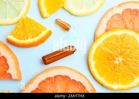 Gebrochene Hautpflegeampulle mit Vitamin C und Scheiben verschiedener Zitrusfrüchte auf hellblauem Hintergrund, flach gelegt Stockfoto