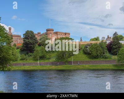 Blick auf eine Burg auf einem Hügel, unter einem ruhigen Fluss mit grünen Ufern und einem Frühlingshimmel, inverness, Schottland, Großbritannien Stockfoto