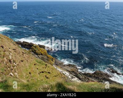 Felsige Küste mit Klippen und Wellen, die unter sonnigem Himmel auf den Felsen krachen, Lerwick, Shetlands, Schottland, Großbritannien Stockfoto