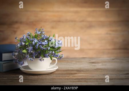 Wunderschöne Vergissmeinsblumen im Becher, Untertasse und Bücher auf Holztisch. Leerzeichen für Text Stockfoto