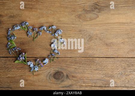 Herz mit wunderschönen Vergissmeint-nicht-Blumen auf hölzernem Hintergrund, Blick von oben. Leerzeichen für Text Stockfoto